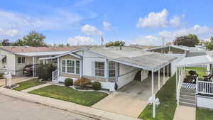 View of front facade featuring an attached carport, concrete driveway, a shingled roof, and a front yard
