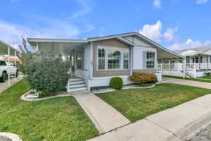 Manufactured / mobile home with a front lawn, a carport, concrete driveway, and a porch