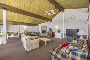 Carpeted living room with high vaulted ceiling, a stone fireplace, a wooden ceiling with exposed beams, and ceiling fan