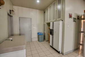 Kitchen with white fridge with ice dispenser, light tile patterned floors, light countertops, and glass insert cabinets