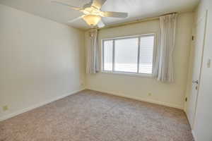 Carpeted empty room featuring baseboards and ceiling fan