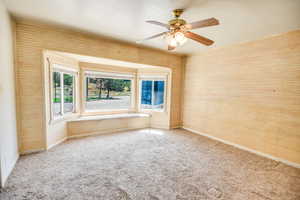Carpeted spare room with a ceiling fan and wood walls