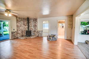 Unfurnished living room with a wood stove, light wood-style floors, ceiling fan, and a textured ceiling