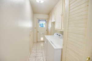 Laundry room with cabinet space, a textured ceiling, washer and clothes dryer, and light tile patterned floors