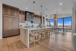 Kitchen featuring a breakfast bar, light stone counters, backsplash, a chandelier, and pendant lighting