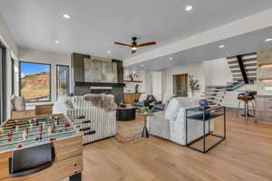 Living area with a tiled fireplace, light wood-style floors, recessed lighting, stairs, and ceiling fan