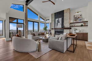 Living area featuring a stone fireplace, high vaulted ceiling, light wood-style flooring, ceiling fan, and beam ceiling