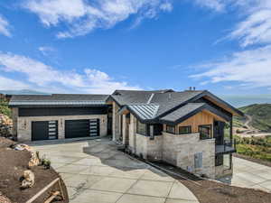Contemporary home with a shingled roof, stone siding, driveway, and a garage