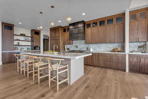 Kitchen with open shelves, tasteful backsplash, glass insert cabinets, a breakfast bar area, and light wood finished floors