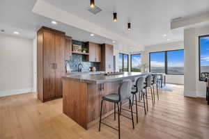 Kitchen with decorative backsplash, a spacious island, brown cabinets, light wood-type flooring, and recessed lighting