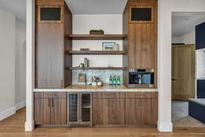 Indoor dry bar with open shelves, modern cabinets, beverage cooler, and brown cabinets