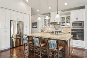 Kitchen featuring glass insert cabinets, appliances with stainless steel finishes, backsplash, white cabinets, and light stone counters