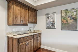 Bar area featuring light stone countertops, dark wood-type flooring, and brown cabinetry