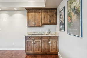 Indoor wet bar with light stone counters, dark wood-style flooring, recessed lighting, and brown cabinetry