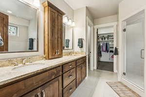 Bathroom with a shower stall, double vanity, light tile patterned flooring, and a spacious closet