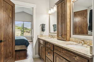 Ensuite bathroom featuring vaulted ceiling, double vanity, and light wood finished floors