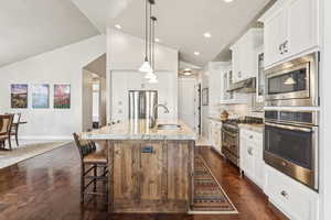 Kitchen with stainless steel appliances, backsplash, pendant lighting, lofted ceiling, and white cabinetry