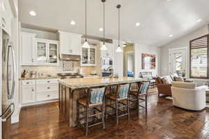 Kitchen featuring glass insert cabinets, tasteful backsplash, white cabinetry, light stone countertops, and a kitchen island with sink