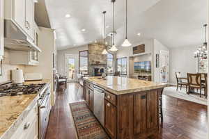 Kitchen with light stone countertops, stainless steel appliances, lofted ceiling, a center island with sink, and dark wood-type flooring