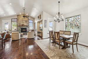 Dining area with vaulted ceiling, dark wood finished floors, a fireplace, a chandelier, and a ceiling fan