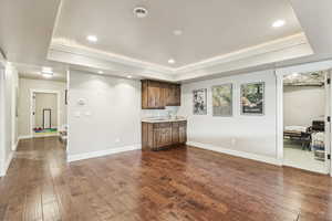 Living room with recessed lighting, dark wood-type flooring, a raised ceiling, and bar with sink