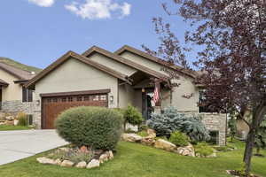 View of front facade featuring stone siding, stucco siding, driveway, a garage, and a front lawn