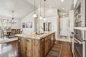 Kitchen with pendant lighting, stainless steel appliances, light stone countertops, a kitchen island with sink, and high vaulted ceiling