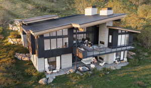 Rear view of house featuring a patio area, stone siding, a chimney, a standing seam roof, and a metal roof