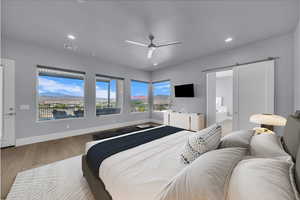 Bedroom with a barn door, light wood-type flooring, recessed lighting, ensuite bathroom, and a ceiling fan