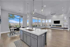 Kitchen with decorative light fixtures, open floor plan, gray cabinetry, a center island with sink, and light wood-type flooring