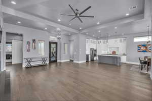 Living room featuring a chandelier, dark wood-type flooring, recessed lighting, ceiling fan, and a raised ceiling