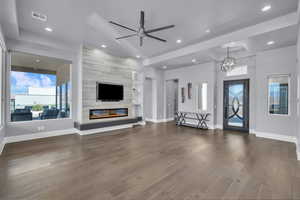 Unfurnished living room featuring dark wood-style floors, ceiling fan, a fireplace, recessed lighting, and a chandelier