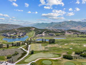 Aerial view of property and surrounding area with a golf course, a water and mountain view, and nearby suburban area