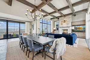 Dining area with a fireplace, beamed ceiling, coffered ceiling, light wood-type flooring, and a chandelier