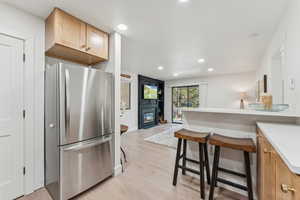 Kitchen featuring freestanding refrigerator, light countertops, light wood-type flooring, recessed lighting, and a kitchen breakfast bar