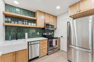 Kitchen with stainless steel appliances, open shelves, light brown cabinets, tasteful backsplash, and recessed lighting