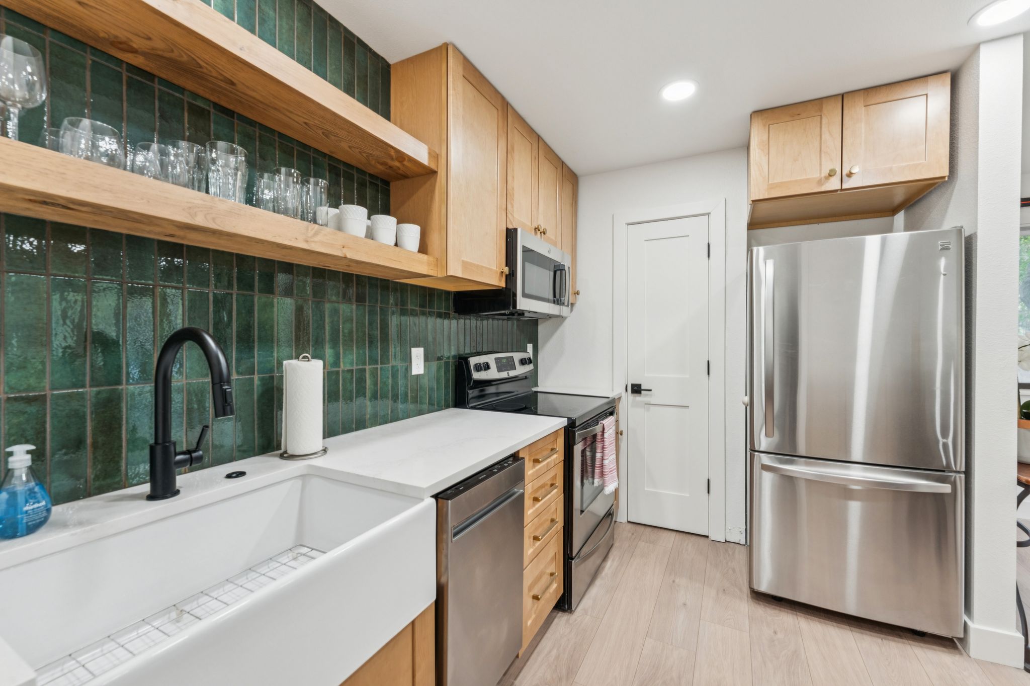 Kitchen featuring open shelves, appliances with stainless steel finishes, tasteful backsplash, light wood-type flooring, and light brown cabinets