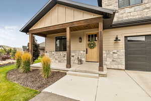 Property entrance with stone siding, board and batten siding, covered porch, and driveway
