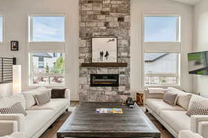 Living room with wood finished floors, a high ceiling, and a stone fireplace