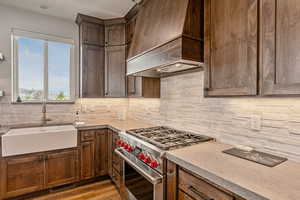 Kitchen with premium stove, custom exhaust hood, light wood-style floors, backsplash, and light stone counters