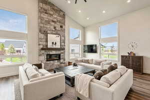 Living area featuring wood finished floors, high vaulted ceiling, a stone fireplace, recessed lighting, and a ceiling fan
