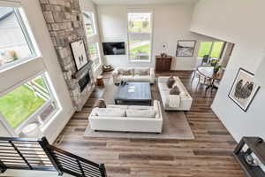 Living room with wood finished floors, a towering ceiling, and a stone fireplace