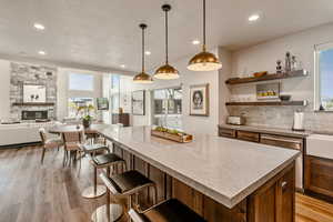 Kitchen with healthy amount of natural light, open floor plan, light wood-style flooring, a stone fireplace, and recessed lighting