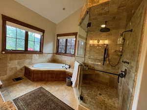 Bathroom featuring vaulted ceiling, a stall shower, a bath, tile walls, and a wainscoted wall
