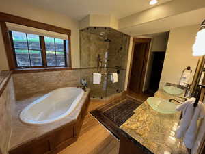 Bathroom featuring a bath, a stall shower, double vanity, and light wood-style floors