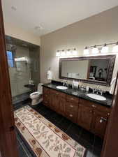 Bathroom featuring a shower stall, double vanity, and dark tile patterned floors