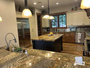 Kitchen featuring hanging light fixtures, backsplash, stainless steel appliances, dark stone countertops, and light wood-type flooring