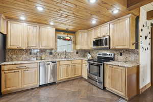 Kitchen featuring light brown cabinetry, stainless steel appliances, backsplash, light stone counters, and wooden ceiling