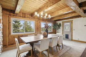Carpeted dining area featuring a wooden ceiling with exposed beams, a chandelier, and wooden walls