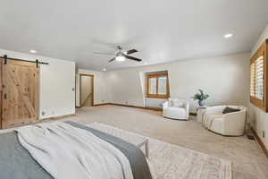 Carpeted bedroom with a barn door, a ceiling fan, multiple windows, and recessed lighting